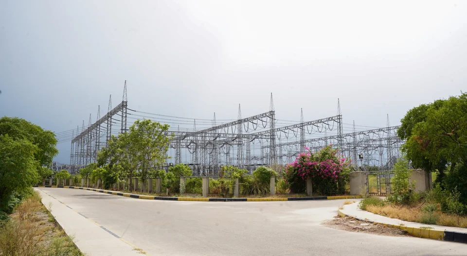 A curving access road beside a grid station, framed by trees and flowering shrubs