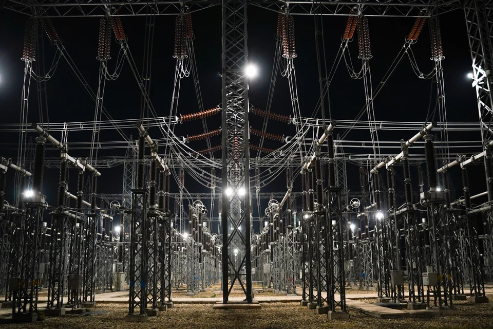 Illuminated steel gantries, insulators and conductors receding through a substation at night