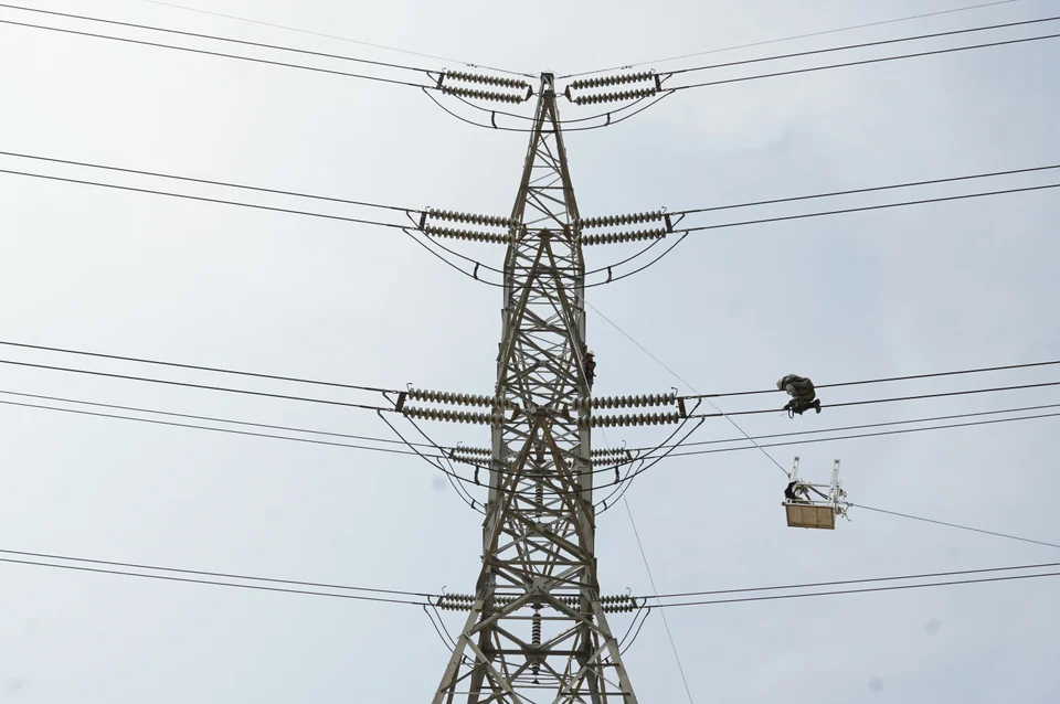 Transmission-line workers beside a steel tower with a suspended work basket